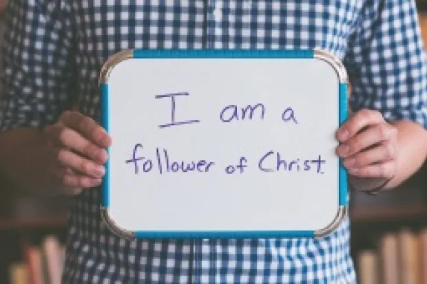 Man holding whiteboard that says "I am a Follower of Jesus"