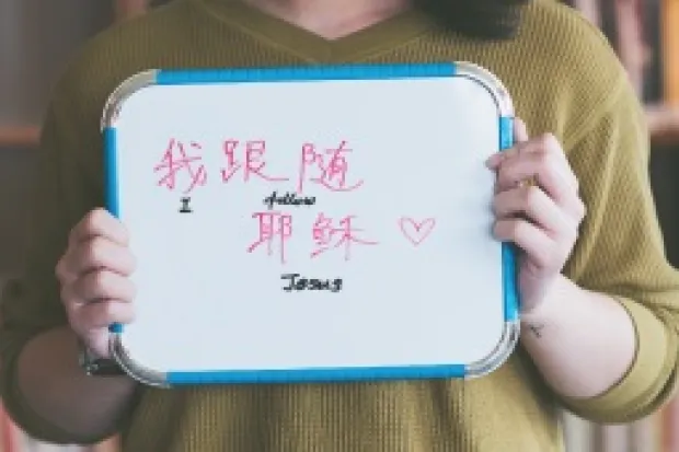 Woman holding whiteboard that says "I am a Follower of Jesus" in English and Chinese characters