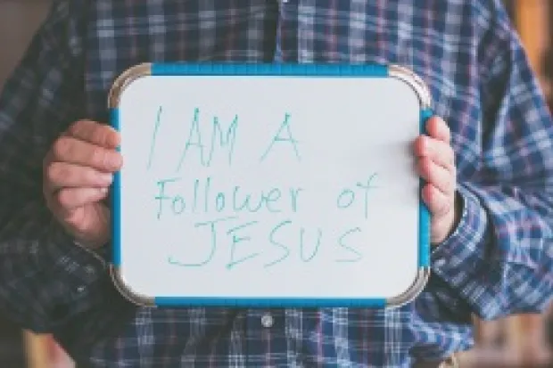 Man holding whiteboard that says "I am a Follower of Jesus"