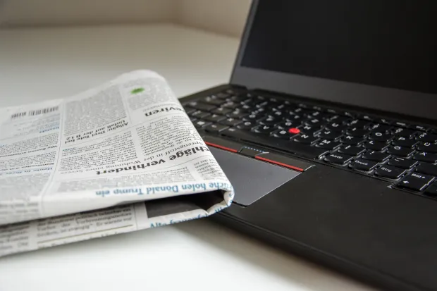 A newspaper resting on the corner of an open laptop computer