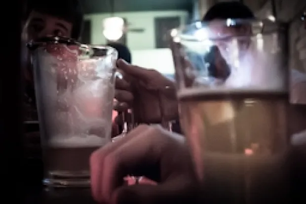 a glass cup half-full with beer and a half-empty beer pitcher on a bar