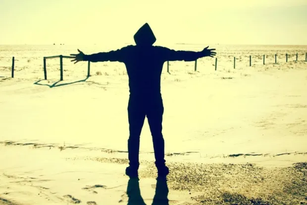 a silhouetted person standing by the water with arms open wide