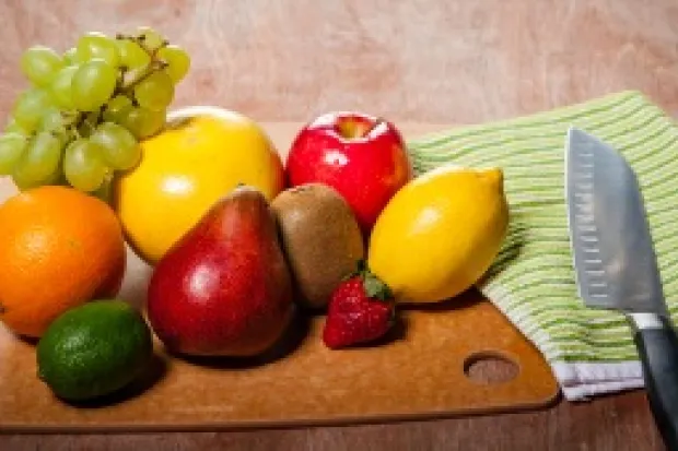 cutting board with fruit such as an orange, apple, lemon, grapes, and others. A cutting knife lies next to it