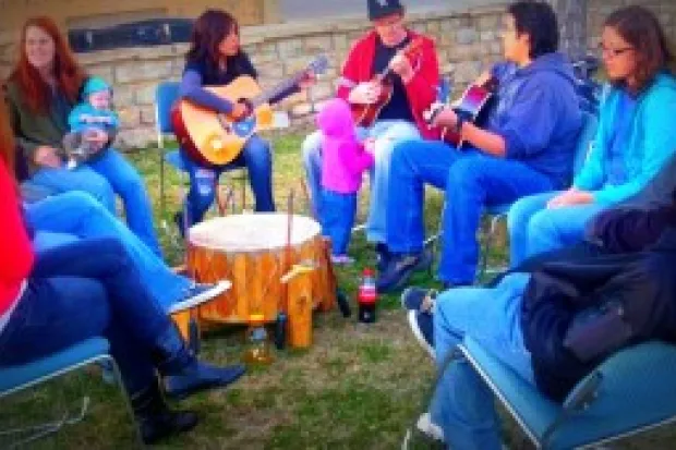 Native family gathering of all ages talking and playing music with guitars and drum