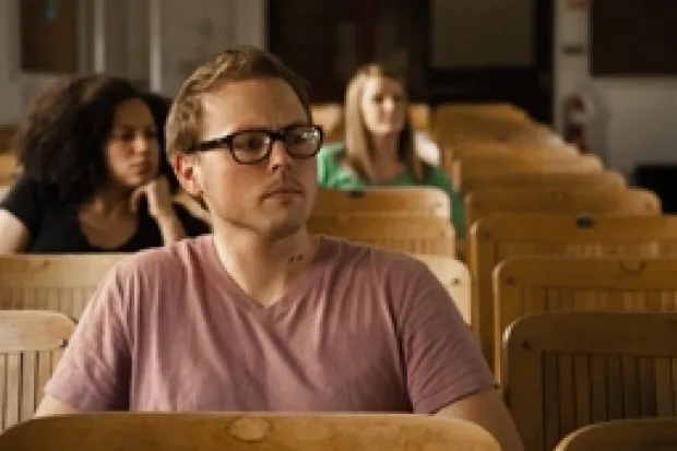 Several students sitting in chairs listening to lecture. Student in front is listening with serious interest.