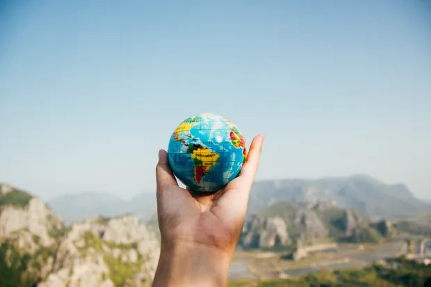 Hand holding small globe against mountain landscape