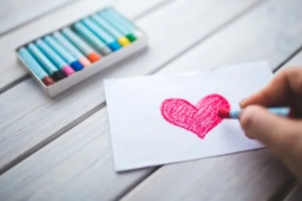 hand coloring a dark pink heart on a small white sheet of paper