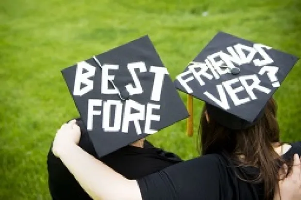 Two college graduates in cap and gown with "Best Friends Forever" written on their caps