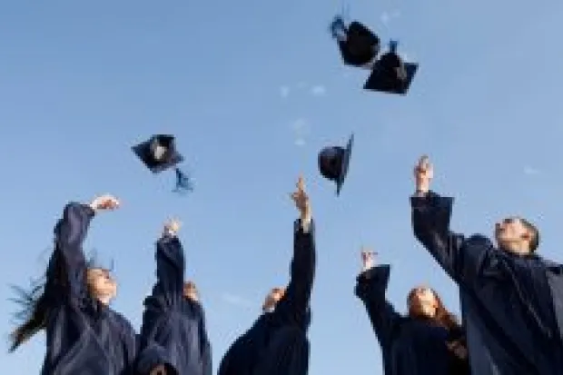 Group of graduates in gowns throwing caps up into air in celebration