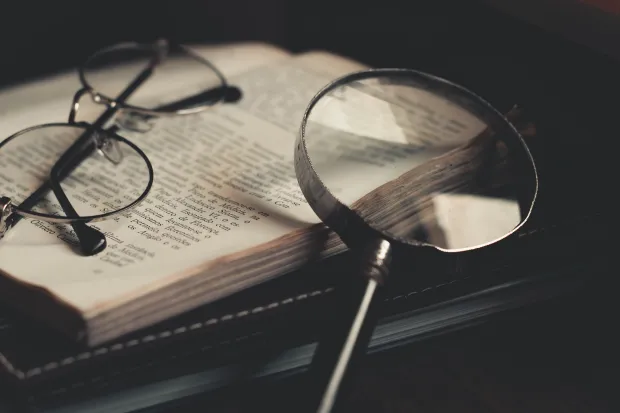 A magnifying glass and eyeglasses resting on a book