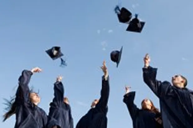 Group of graduates in gowns throwing caps up into air in celebration