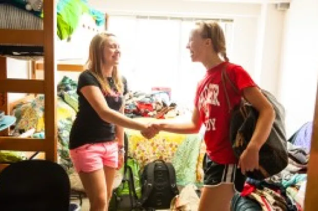 Two students shaking hands in a dorm room