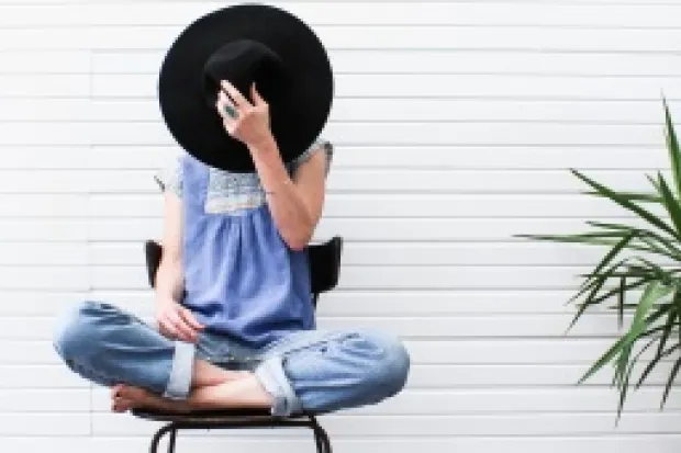woman sitting cross-legged with a wide-brim hat covering her face