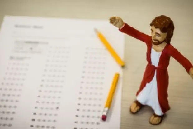 Jesus action figure standing next to standardized test and broken pencil