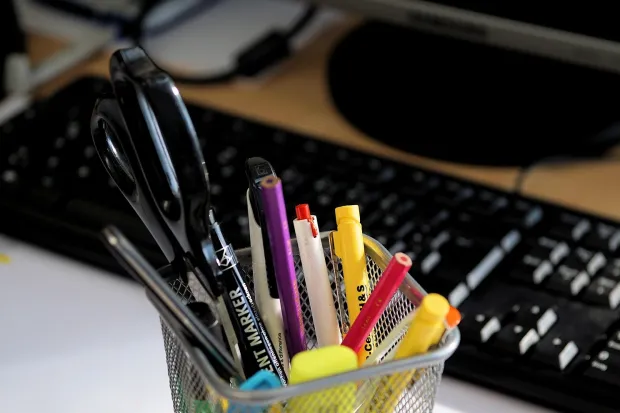 a variety of colorful pens in a cup resting in front of a computer keyboard