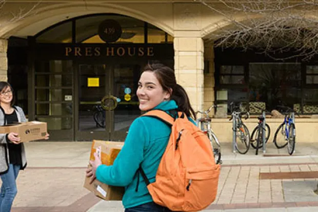 Student and mother walking with boxes toward campus building