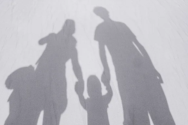 the shadow of two adults holding the hand of a child