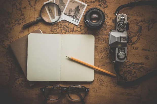  A pencil on white notebook near eyeglasses and a camera