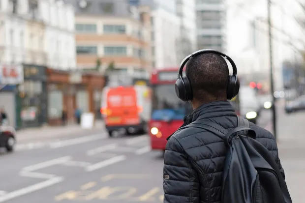 Closeup of young man wearing headphones standing on city street corner