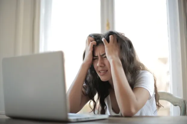 Woman cradling head in frustration, staring at computer