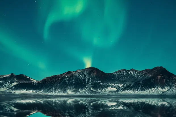 Green and blue Northern Lights shimmering above mountain and lake landscape