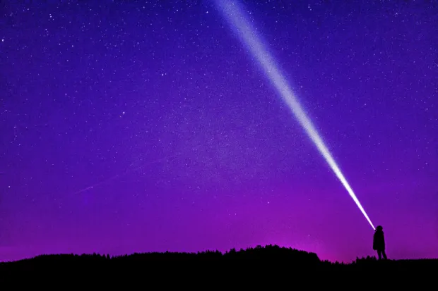 Person outside at night shining flashlight into purple sky