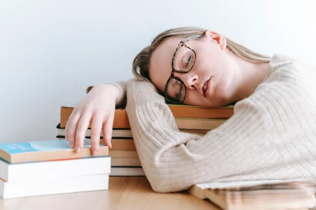 Young woman taking nap on stack of books on top of desk