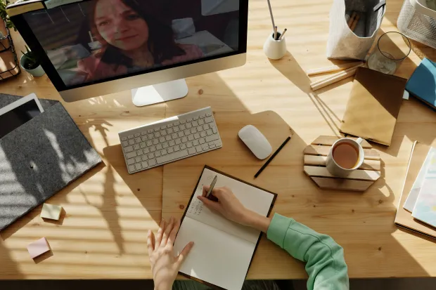 Person sitting at cluttered desk in front of computer taking notes