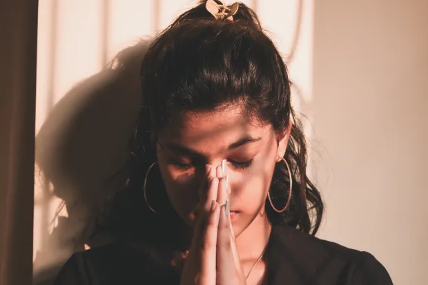 a young woman praying with her hands folded in front of her face