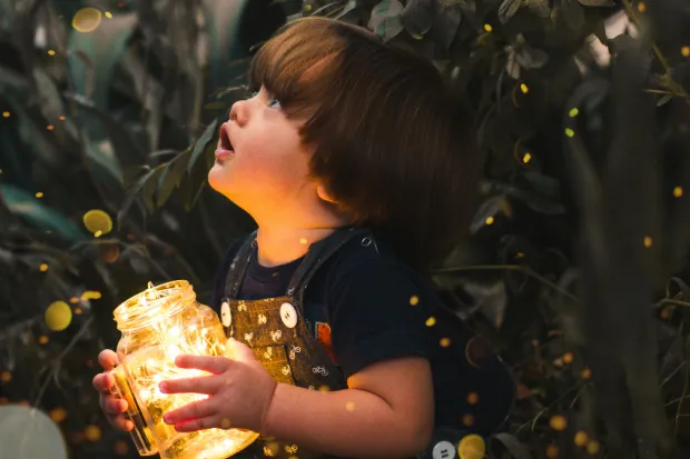 Child holding jar full of fireflies staring up into sky