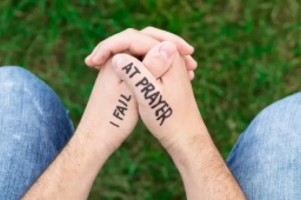 Person's hands folded for prayer with the words: "I Fail at Prayer" written on hands in marker.