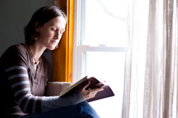 a woman reading a Bible next to a sunlit window