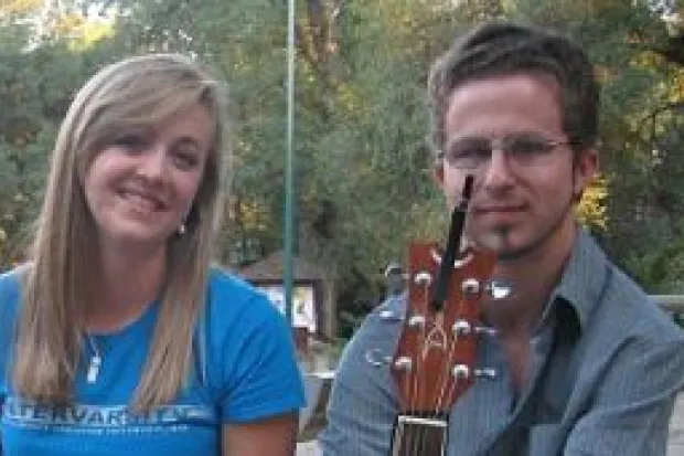 Young woman smiling seated on bench next to young man with guitar