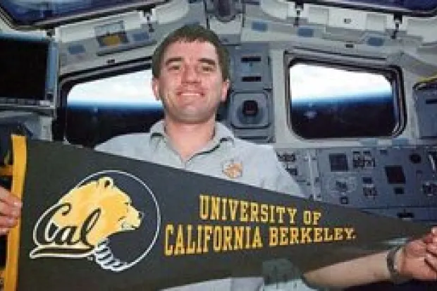 Rex Walheim holding a University of California, Berkeley Banner in space shuttle cockpit