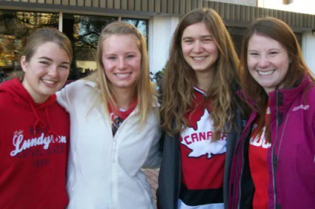 Group of four young female students arm in arm smiling outside of dorm