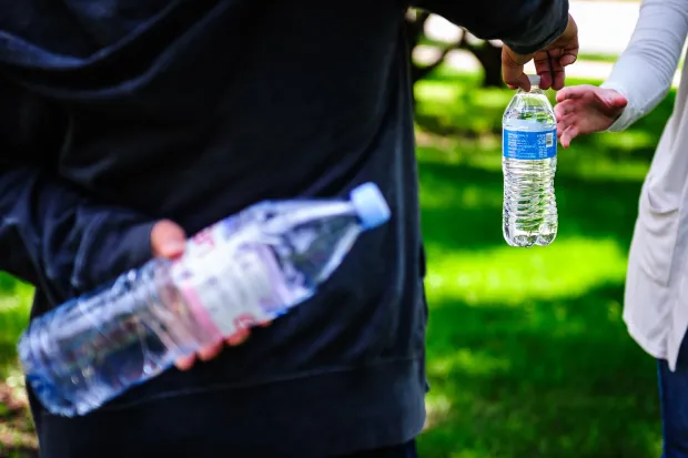 Person handing someone a bottle of water while holding another bottle behind back