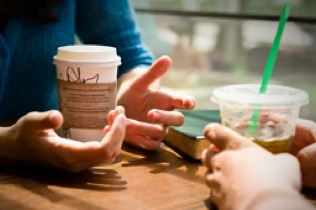 Closeup of two people's hands holding coffee tumblers on table