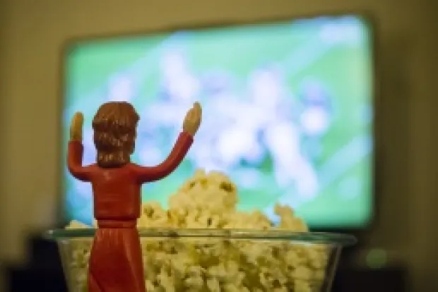 Jesus action figure in front of popcorn bowl facing TV