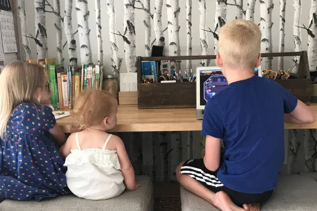 three small children sitting at a countertop using a computer