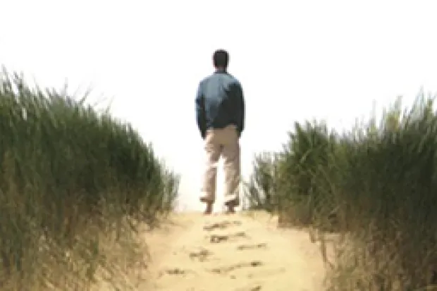 Back of young man staring off into the distance on beach with footprints in sand