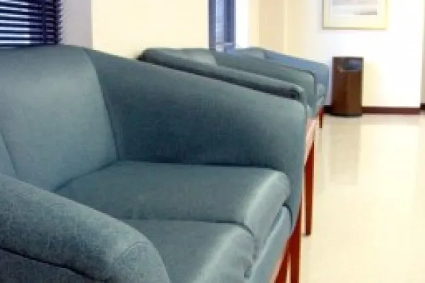 A gray leather couch sitting in a hallway with smooth concrete floors.