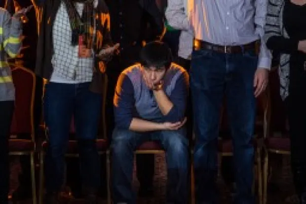 a sad-looking man sitting down in a crowd of standing people