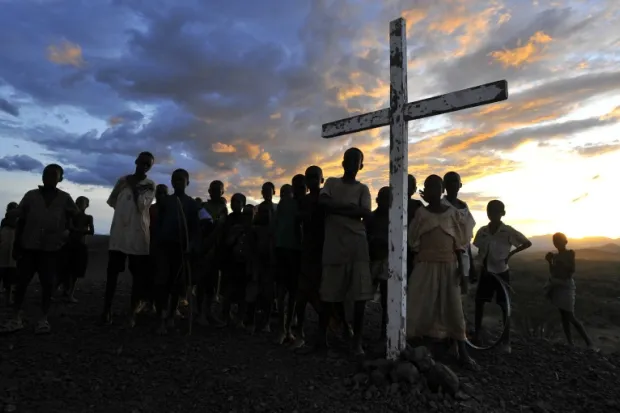 Wooden cross surrounded by group of children with sunset in the background