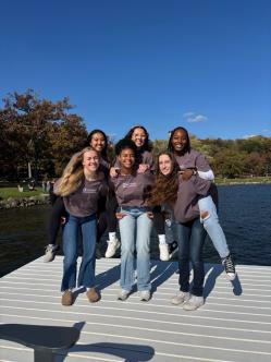 group of female students smiling for a photo by the lake