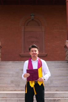 Joseph holding his diploma outside in front of a building