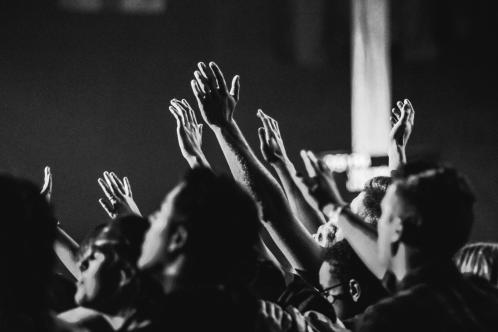 A black and white photo of many hands raised in worship