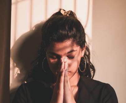 a young woman praying with her hands folded in front of her face