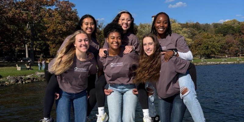 group of female students smiling for a photo by the lake
