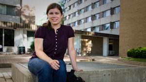 a female student sitting on a fountain in front of a dormitory building