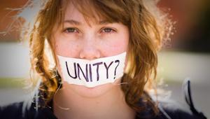 Closeup of woman with paper over mouth with the word: Unity?